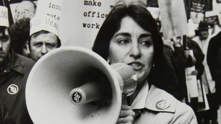 Black and white publicity still from 9TO5: THE STORY OF A MOVEMENT (2020). Karen Nussbaum marches for equal pay. 1970s