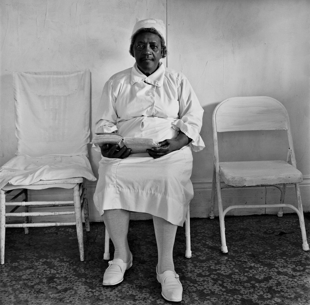 Sister Gertrude Morgan is seated against a white wall within her mission located in New Orleans, LA.
