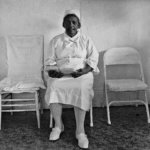 Sister Gertrude Morgan is seated against a white wall within her mission located in New Orleans, LA.