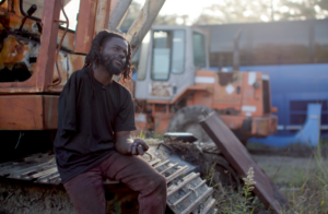 A man sits on a steam shovel, being interviewed.